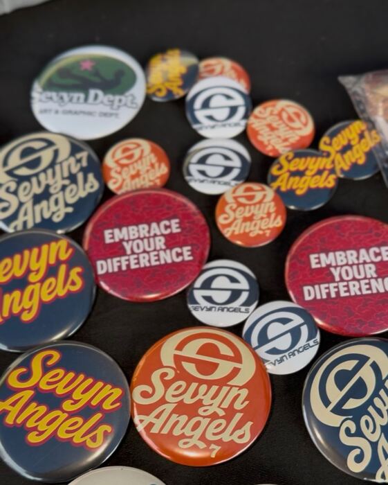 Pile of custom pin-back buttons with an organization logo in red, navy and cream