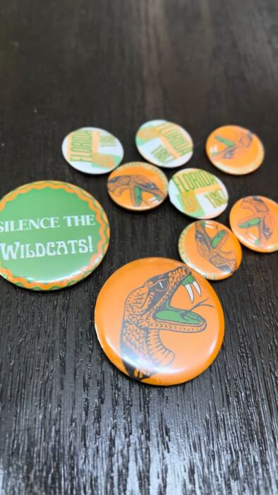 Orange and green school spirit pin-back buttons on a dark table