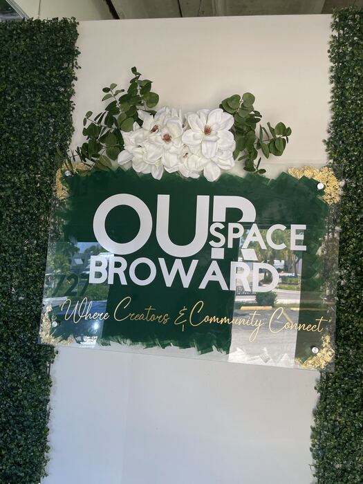 Green acrylic business wall sign with white and gold lettering and white flowers on top