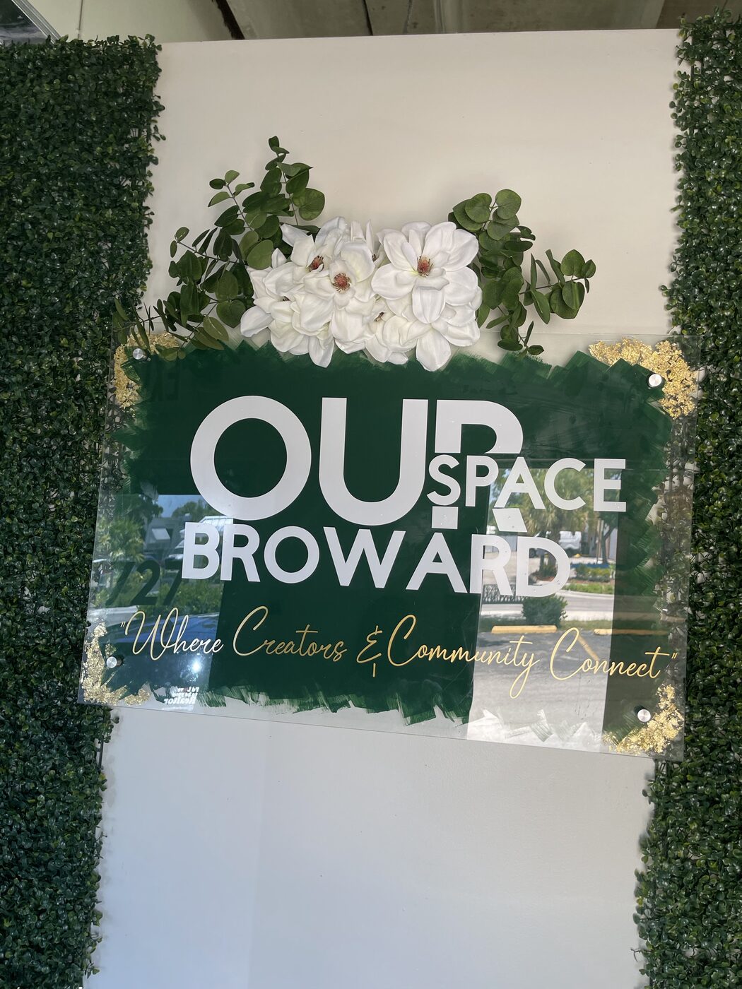 Green acrylic business wall sign with white and gold lettering and white flowers on top