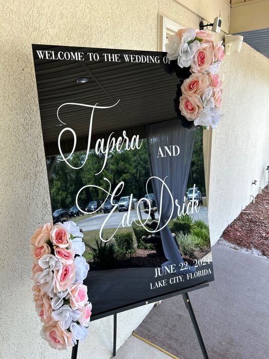 Black acrylic wedding welcome sign with white script names and pink and white roses on an easel